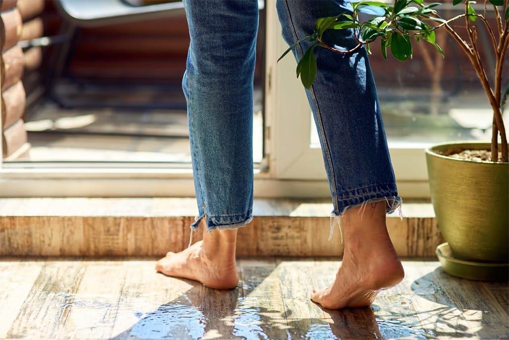 Balkon undicht – Frau barfuß auf feuchtem Balkon – Wasserschaden Göttingen Frau geht barfuß auf feuchtem Balkon und Wohnungsboden – undichte Balkonfläche als Ursache für Wasserschaden in der Wohnung in Göttingen